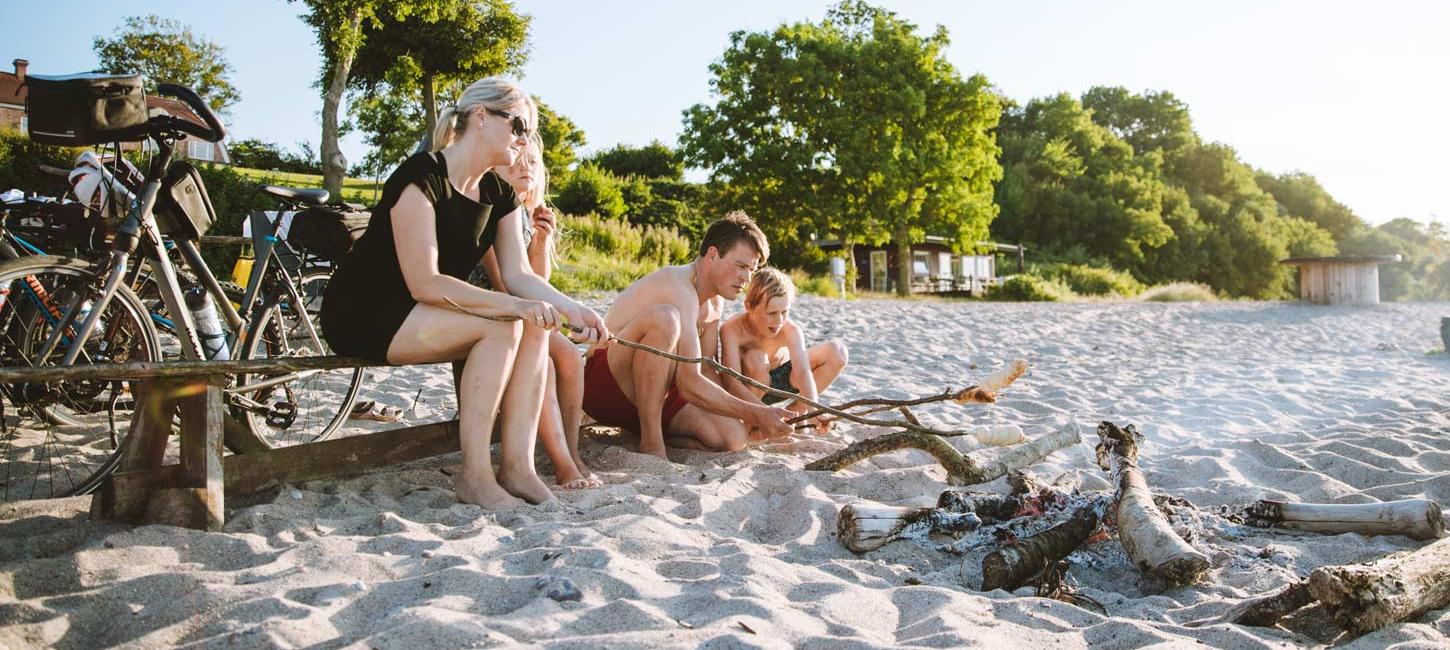Familie på stranden med cykler og bål