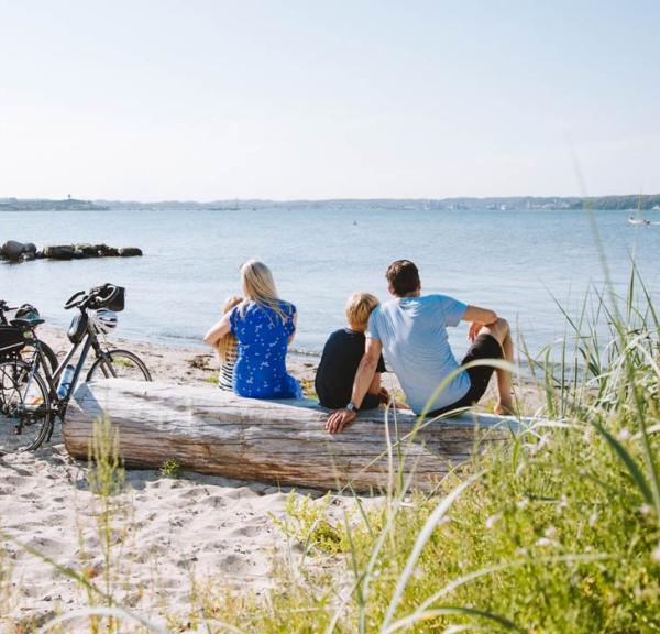 Familie sitzt mit Fahrrädern am Strand und schaut aufs Wasser 